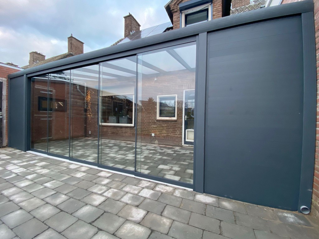 Referenz Oberbayern: Aluminium-Terrassenüberdachung in Anthrazit mit Glasschiebewänden und seitlicher Aluminium-Wand an einem Einfamilienhaus